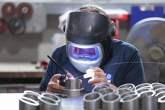 Männlicher Facharbeiter beim Schweißen von Metallkomponenten mit Schutzmaske in der industriellen Fertigung.