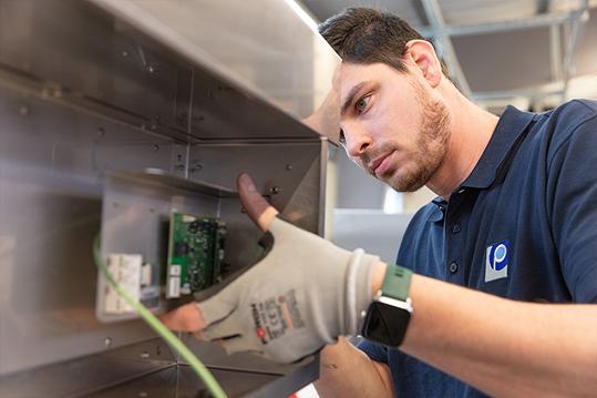 Männliche Fachkraft in blauem Poloshirt und Schutzhandschuhen montiert technisches Bauteil in Werkstatt