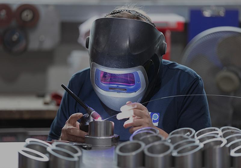 Männlicher Facharbeiter beim Schweißen von Metallkomponenten mit Schutzmaske in der industriellen Fertigung.