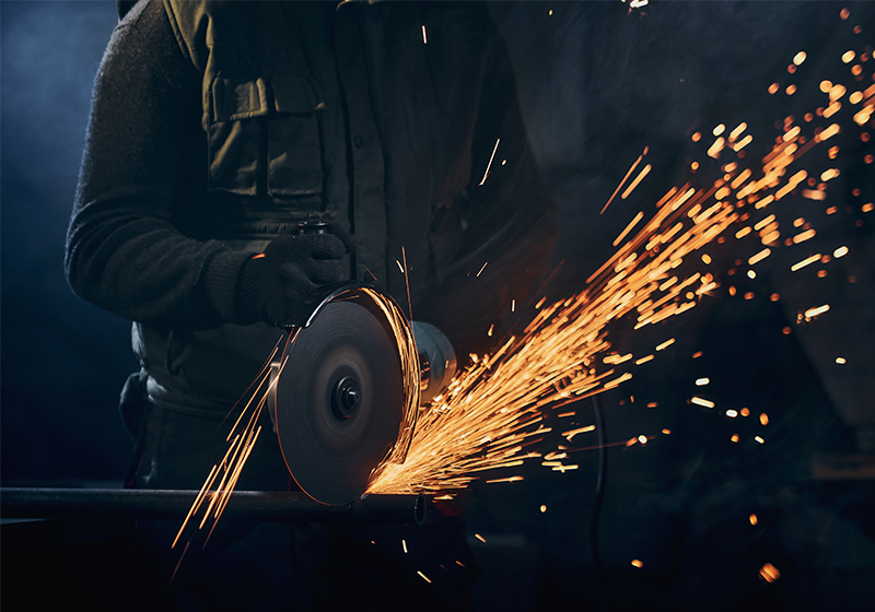 Männlicher Facharbeiter beim Schleifen von Metallkomponenten mit Schutzkleidung in der industriellen Fertigung. Männlicher Facharbeiter beim Schleifen von Metallkomponenten mit Schutzkleidung in der industriellen Fertigung.