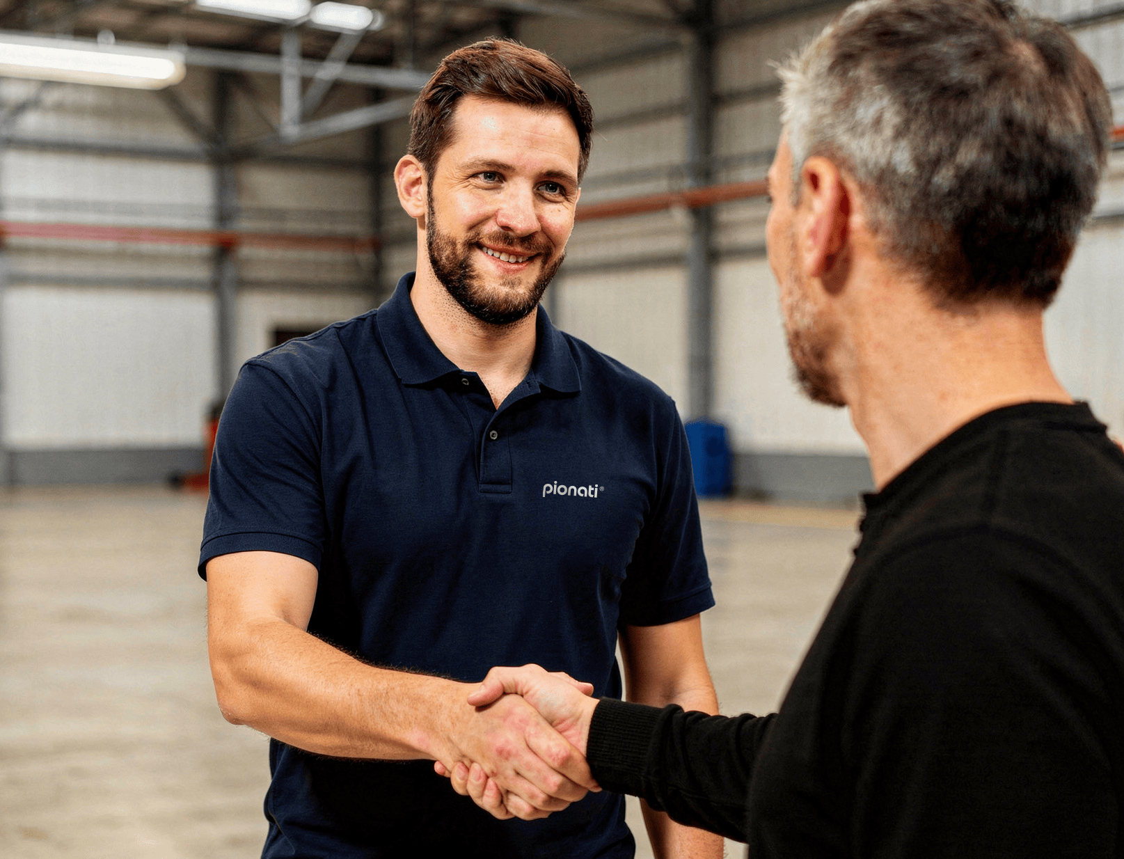 Mitarbeiter in dunkelblauem Poloshirt begrüßt Kunden bei einem persönlichen Gespräch im Logistik- oder Produktionsumfeld.